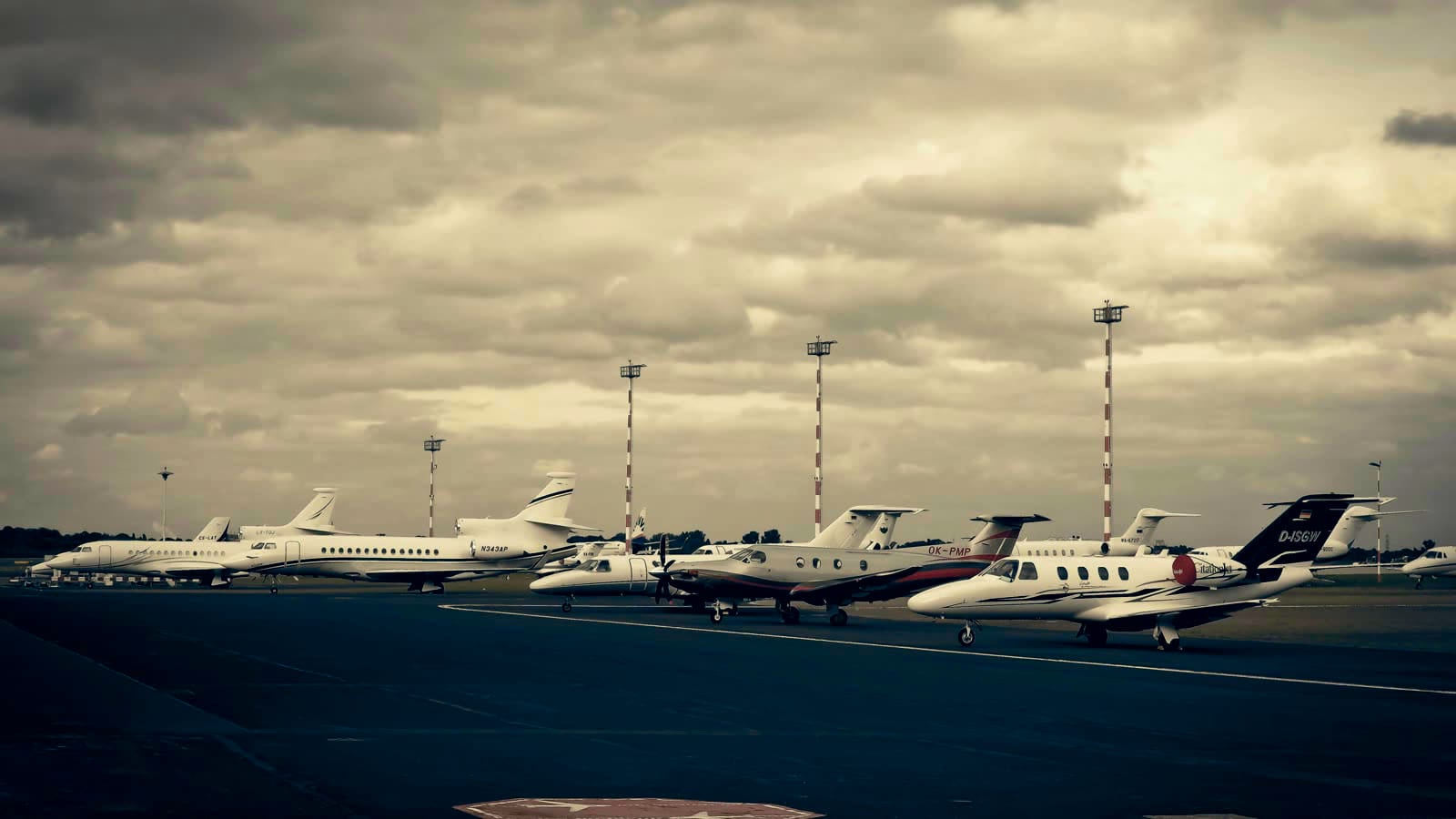 Fila de jets ejecutivos en plataforma bajo un cielo cargado